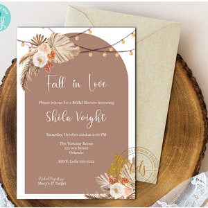 Puede incluir: Una invitación a una despedida de soltera con temática otoñal. La invitación presenta un fondo marrón con un borde blanco y un texto que dice "Caer en el amor". La invitación también presenta un diseño floral con hojas de palma secas y luces de cadena.