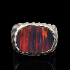 May include: A silver ring featuring a large, oval-shaped black opal gemstone with vibrant red and orange flashes of color. The metal band has a textured, scalloped edge surrounding the stone, creating a distinct frame for the dark, iridescent gem.