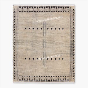 Peut inclure: Un tapis rectangulaire beige avec un motif géométrique. Le tapis présente des motifs de losanges noirs et de lignes verticales, avec une bordure de triangles et un bord supérieur décoratif. Le texte "VINTAGEFLOORINGRUG" est visible.