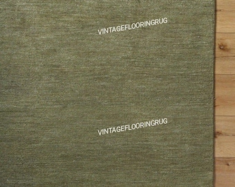 Pode incluir: Tapete verde-oliva com superfície texturizada e borda com franjas. O texto "VINTAGEFLOORINGRUG" está impresso no tapete. O tapete está colocado sobre um chão de madeira.