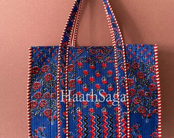 May include: A blue tote bag with a floral pattern in red and white. The bag has matching handles and trim. The text "Haath Saga" is visible on the front of the bag.