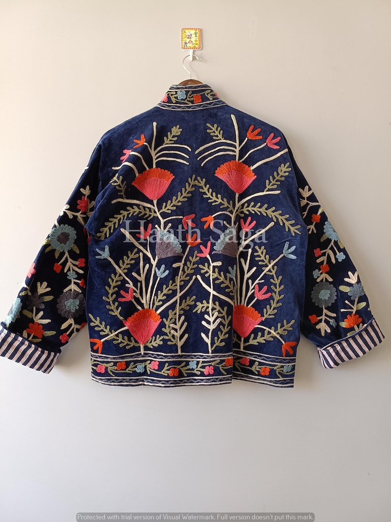 May include: A navy blue jacket with intricate floral embroidery in red, orange, green, and blue. The jacket features a relaxed fit, long sleeves, and striped cuffs. The back of the jacket displays the text "Haath Saga".