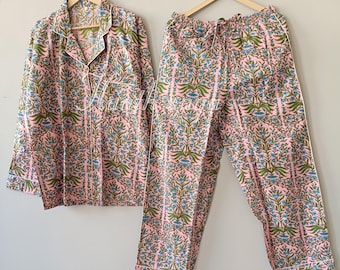 May include: A pink floral pajama set, comprising a collared, button-down shirt and matching trousers with a drawstring waist. The floral pattern incorporates blue and green elements. The set is designed for comfort and relaxation.