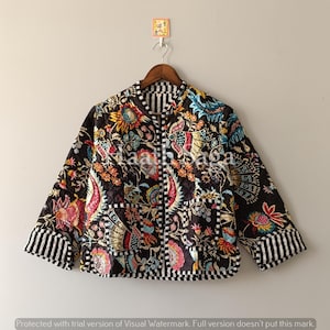 May include: A black quilted jacket with a colourful floral design in red, blue, yellow, and green. The jacket features striped trim on the collar, cuffs, and hem. The text "Shaali Saga" is visible on the jacket.