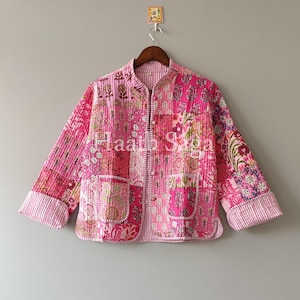Op de afbeelding: Een gewatteerde roze jas met een bloemen patchwork ontwerp. De jas heeft lange mouwen, twee voorzakken en een knoopsluiting. De manchetten en kraag zijn gestreept. De tekst "Haath Saga" is zichtbaar.