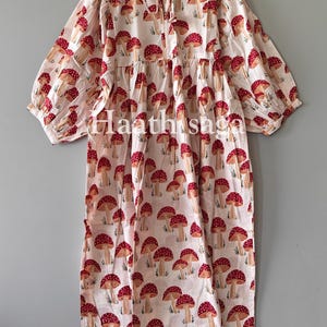 May include: A white dress with a red mushroom pattern. The dress has a round neckline, long sleeves, and a loose, flowing fit. The text "Haathisaga" is visible on the dress.
