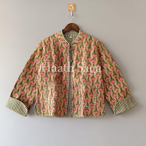 Può includere: Giacca trapuntata con motivo floreale rosa e verde. La giacca ha un colletto alla coreana, due tasche frontali e polsini a righe. Il testo "Haath Saga" è visibile.