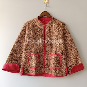 May include: A leopard print jacket with red trim and pockets. The jacket has a zip-up front and is hanging on a wooden hanger. The jacket's pattern is brown and tan with red accents. The text "Haath Saga" is visible on the jacket.