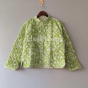 May include: A lime green quilted jacket with a white floral pattern. The jacket has a mandarin collar, two front pockets, and a full-length zip. The jacket is hanging on a wooden hanger against a grey background. The text "Haathisingh" is visible on the jacket.