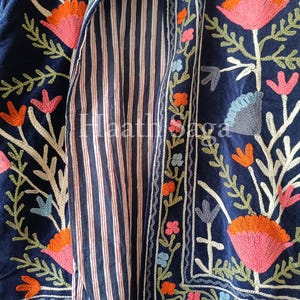 May include: A navy blue embroidered jacket with a striped interior. The jacket features floral embroidery in shades of pink, orange, and blue. The interior lining has vertical red and white stripes.
