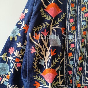 May include: A navy blue jacket with intricate floral embroidery in shades of pink, orange, and blue. The jacket features a detailed design with a mix of embroidered flowers and leaves, and the text "Haath Saga".