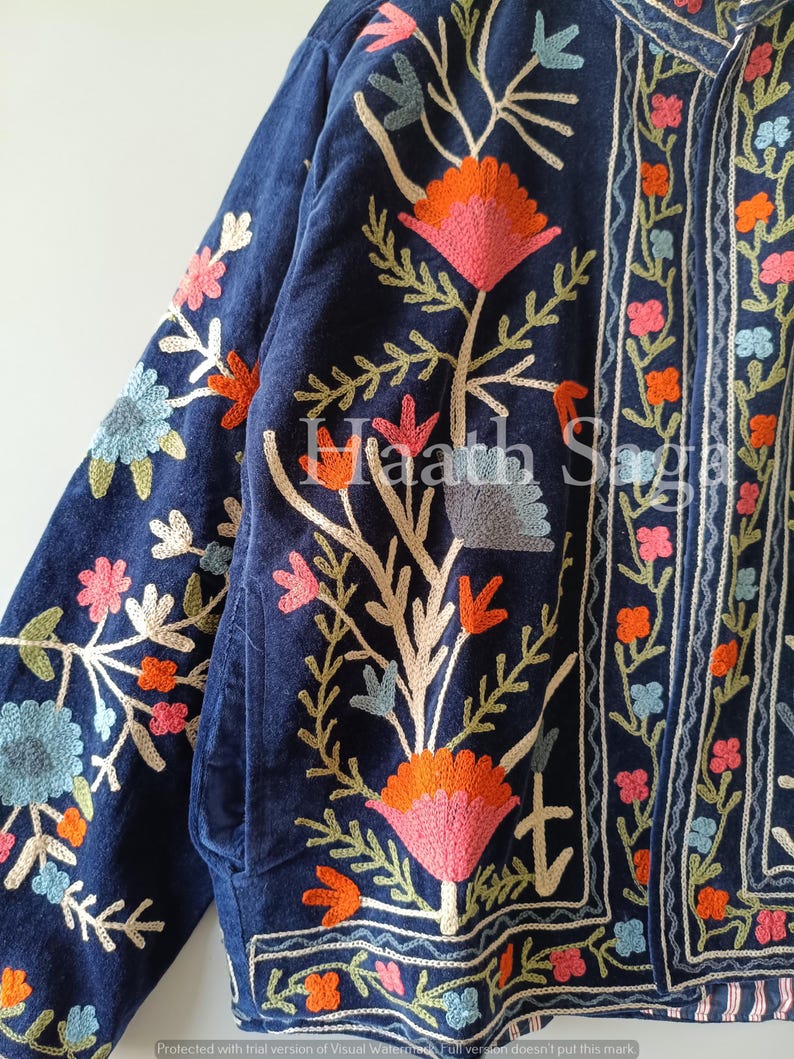 May include: A navy blue jacket with intricate floral embroidery in shades of pink, orange, and blue. The jacket features a detailed design with a mix of embroidered flowers and leaves, and the text "Haath Saga".