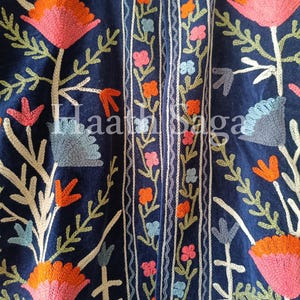 May include: Close-up of a navy blue textile with intricate floral embroidery. The design features large pink and orange flowers, green leaves, and smaller flowers in pink, orange, and blue. The text "Haath Saga" is visible.