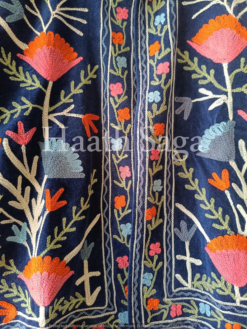 May include: Close-up of a navy blue textile with intricate floral embroidery. The design features large pink and orange flowers, green leaves, and smaller flowers in pink, orange, and blue. The text "Haath Saga" is visible.