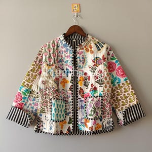 Puede incluir: Chaqueta acolchada con un vibrante estampado floral y de mariposas. La chaqueta presenta una mezcla de colores, incluyendo rosa, azul y verde, con detalles a rayas blancas y negras en los puños y el ribete. Tiene cuello mandarín y cremallera negra.