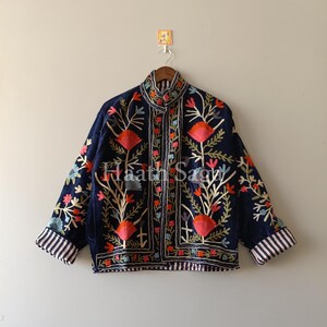 May include: A navy blue jacket with intricate floral embroidery in shades of red, orange, pink, and green. The jacket features a high collar and striped cuffs. The text "Haath Sagy" is visible on the jacket.