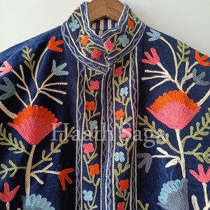 May include: A dark blue jacket with intricate floral embroidery in shades of pink, orange, and blue. The jacket features a high collar and a detailed pattern of flowers and leaves. The text "Haathi Saga" is visible on the jacket.