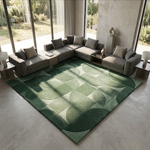 Op de afbeelding: Een groot, rechthoekig vloerkleed met een geometrisch patroon van overlappende cirkels en vierkanten in verschillende tinten groen. Het kleed heeft een getufte, textuurrijke pool en ligt op een lichtgrijze betonnen vloer.