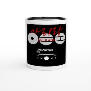 May include: White ceramic mug with a black interior and a black exterior design. The design includes Korean text in red, three white circles, and the text "ARIRANG" in white. Below, the text "Like Animals" and "BTS" are displayed.