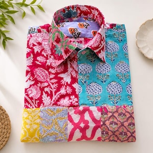 Può includere: Una camicia a maniche lunghe con bottoni caratterizzata da un design patchwork con vari motivi floreali e geometrici in colori vivaci, tra cui magenta, turchese, giallo e rosa. Il colletto e i pannelli frontali presentano motivi stampati a contrasto.