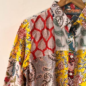 Op de afbeelding: Een overhemd met lange mouwen en knoopsluiting met een levendig patchworkontwerp met diverse bloemen-, paisley- en bladpatronen in tinten geel, rood, blauw en wit. Het overhemd heeft een standaard kraag, witte knopen en een maat M label in de nek.