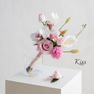 May include: A floral arrangement featuring pink roses, tulips, and calla lilies, presented in a clear glass. A single rose and foliage rest on a white surface. The word "Kiss" is written in cursive.