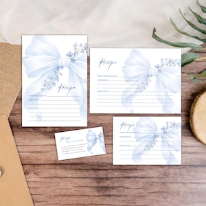 Puede incluir: Un conjunto de tarjetas de recetas con un diseño de acuarela. Cada tarjeta presenta un lazo azul claro y detalles florales. Las tarjetas están dispuestas sobre una superficie de madera, con la palabra "Receta" impresa en cada tarjeta.