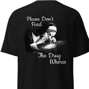 以下が含まれることがあります： 黒いTシャツ。修道女が薬物を吸引している白黒のグラフィック。画像の上には「Please Don't Feed」、下には「The Drug Whores」というテキストがあります。