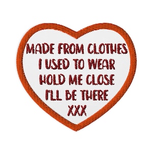 Puede incluir: Parche bordado en forma de corazón con centro blanco y borde rojo. El parche presenta el texto "MADE FROM CLOTHES I USED TO WEAR HOLD ME CLOSE I'LL BE THERE XXX" en letras rojas. Diseñado para coser en la ropa.