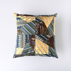 May include: A square pillow with a patchwork design made from different patterned fabrics in shades of blue, green, yellow, and brown.