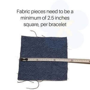 May include: A square piece of dark blue denim fabric measuring 2.5 inches across, as indicated by a white measuring tape placed horizontally over the material. The text above reads: Fabric pieces need to be a minimum of 2.5 inches square, per bracelet.