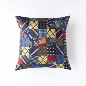 May include: Square decorative pillow with a patchwork design made from various patterned neckties. The pillow features a mix of colors including blue, yellow, red, and green. The patchwork is arranged in a grid pattern, creating a unique and textured appearance.