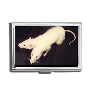 May include: A silver cigarette case featuring a black background with two white rats. The rats have pink eyes and long whiskers. The case has a shiny, metallic finish and a rectangular shape.