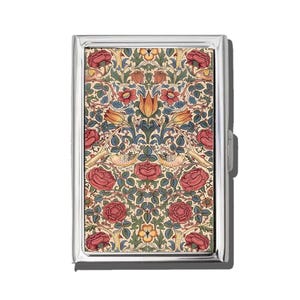 May include: A silver metal cigarette case with a colorful floral pattern. The design features red roses, yellow birds, and orange tulips on a cream background. The case has a rectangular shape and a clasp closure.
