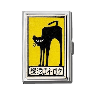 May include: A silver metal cigarette case featuring a black cat silhouette on a yellow background. The cat is arched with its tail up. Japanese text is at the bottom of the yellow rectangle. The case has a silver metal frame and a clasp.