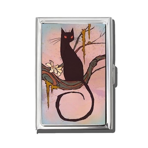 May include: A silver metal cigarette case featuring a black cat with red eyes perched on a tree branch. The illustration has a whimsical style with a pink and blue background and a white flower.