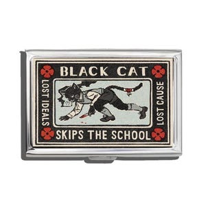 May include: A silver metal cigarette case featuring a vintage illustration of a black cat holding a knife, with text that reads "BLACK CAT" and "SKIPS THE SCHOOL". The design includes red floral accents and the phrases "LOST IDEALS" and "LOST CAUSE".