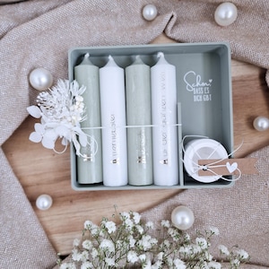 Puede incluir: Un juego de cuatro velas de pilar en tonos verde salvia y blanco, dispuestas en una bandeja rectangular. Las velas están adornadas con letras doradas y atadas con una cuerda blanca. La bandeja incluye el texto "Schön, dass es dich gibt."