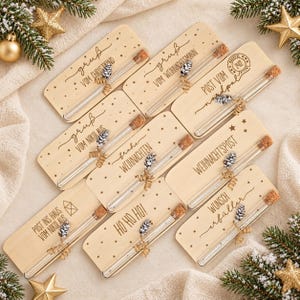 Könnte beinhalten: Acht rechteckige Holzschilder mit abgerundeten Ecken, jedes mit einem klaren Glasreagenzglas und Korkverschluss. Jedes Schild ist mit deutschem Weihnachtstext, kleinen Sternen und einem kleinen, mit Bindfaden befestigten Tannenzapfen versehen.
