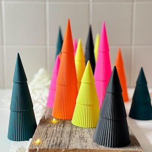 Peut inclure: Une collection d'arbres décoratifs coniques colorés dans diverses nuances de vert, orange, rose, jaune et noir. Les arbres sont disposés sur une base en bois rustique, créant un affichage vibrant et moderne. Les arbres ont une texture côtelée.