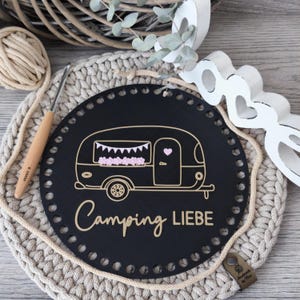 Könnte beinhalten: Ein runder schwarzer Holzboden mit einer Reihe von Löchern am Rand, verziert mit einer goldfarbenen Umrisszeichnung eines Wohnwagens, einem kleinen rosa Herz und dem Schriftzug "Camping LIEBE" in goldener Schreib- und Blockschrift.