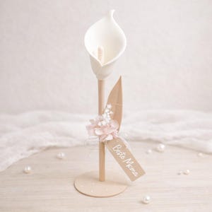 Könnte beinhalten: Ein Set aus drei Keramikbechern mit einer gesprenkelten, cremefarbenen Glasur. Jeder Becher hat ein anderes handgemaltes Design: ein blaues und grünes Blatt, eine gelbe Blume und eine rote Beere. Die Becher haben ein schlichtes, modernes Design.