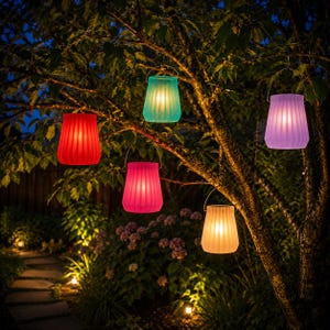 May include: A nighttime outdoor scene features a tree adorned with five colorful, glowing lanterns. The lanterns, in shades of red, teal, pink, purple, and yellow, are suspended from branches, illuminating a garden path and foliage.