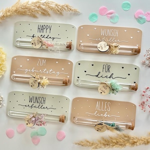 Puede incluir: Seis placas decorativas de madera con tubos de vidrio y tapones de corcho. Cada placa tiene un mensaje diferente en escritura cursiva, como "HAPPY birthday" y "WUNSCH erfüller". Las placas están decoradas con pequeñas etiquetas de madera y flores secas.