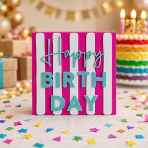 Może przedstawiać: Prostokątny znak w pionowe paski w kolorze intensywnego różu i bieli z napisem "Happy BIRTH DAY" wypukłymi, jasnoniebieskimi literami. Znak jest ustawiony pionowo, prezentując odważny, kolorowy wzór z wyraźną, warstwową typografią.