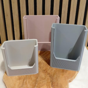 以下が含まれることがあります： パステルカラーの長方形収納容器3つ。容器はグレー、ピンク、ブルーの色合いです。各容器の底には垂直のリブデザインがあります。容器は木製の表面に表示されています。