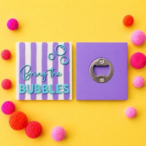 May include: A square bottle opener with a purple and white striped front featuring the teal text "Bring The BUBBLES" and three teal circles. The back is solid purple with a centered metal bottle opener mechanism, surrounded by small colorful pom-poms.