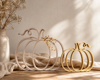 May include: Two open-frame pumpkin decorations made of thin, smooth material. The larger pumpkin is a light beige colour, while the smaller pumpkin is a metallic gold colour. Both feature curved stems and vertical ribs forming a hollow silhouette.
