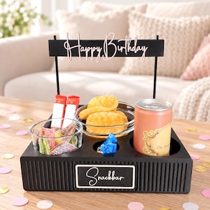 Könnte beinhalten: Ein schwarzes, rechteckiges Snack-Tablett mit einem vertikalen Schild mit der Aufschrift Happy Birthday und einem Etikett mit der Aufschrift Snackbar. Das Tablett enthält eine Glasschale mit Fruchtgummis, Kartoffelchips und eine Getränkedose.