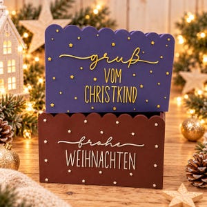 May include: Two stacked rectangular wooden boxes with scalloped top edges. The top purple box features yellow text reading "gruß VOM CHRISTKIND" with small yellow stars. The bottom brown box features white text reading "frohe WEIHNACHTEN" with small white stars.